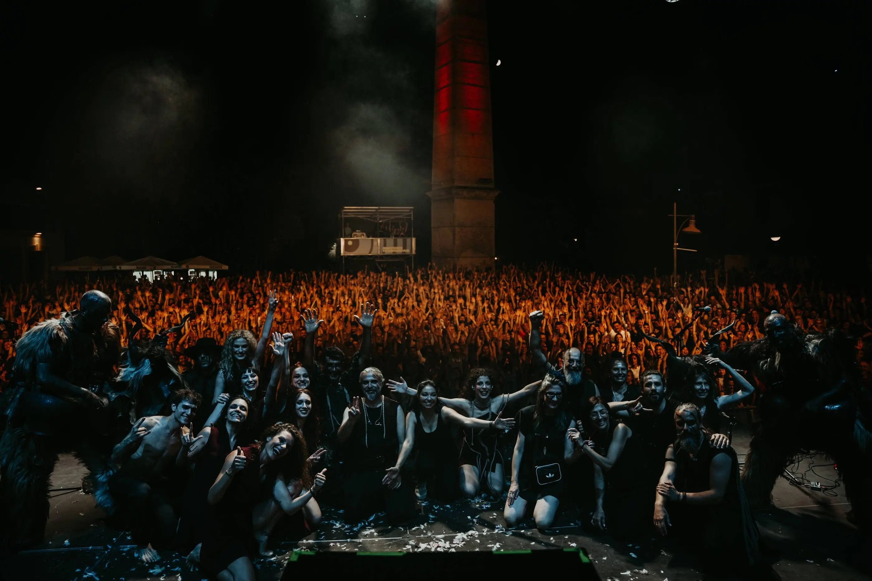 The band seated at the front of the stage with thousands of people behind them
